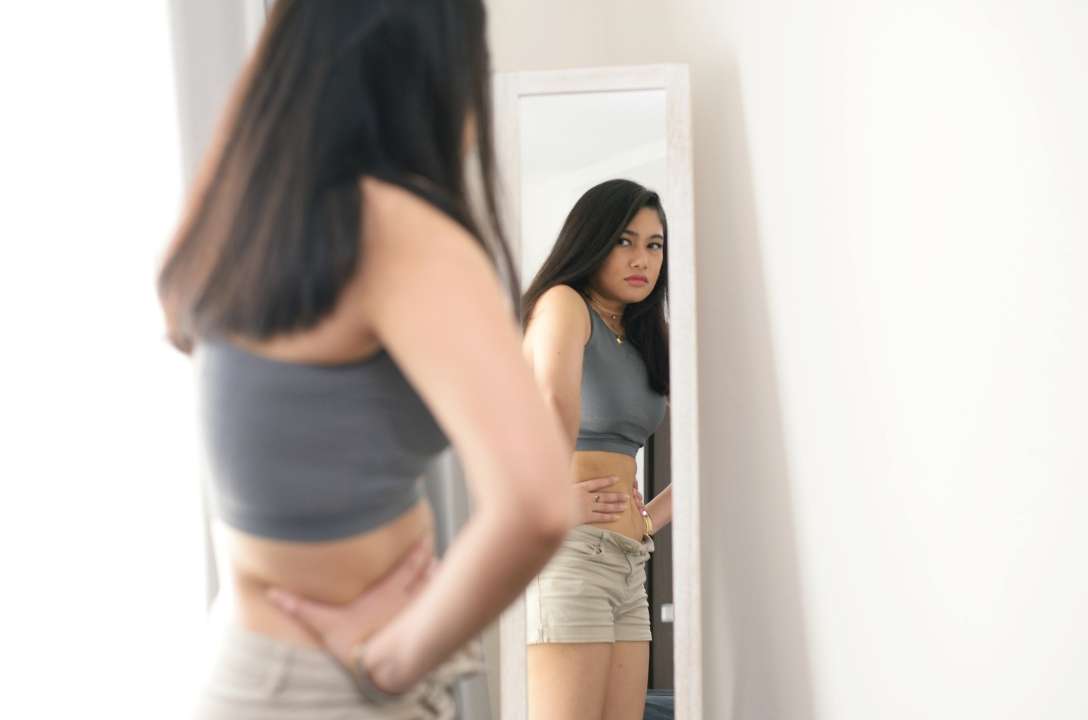 Girl looking in the mirror frowning unhappy due to poor body image