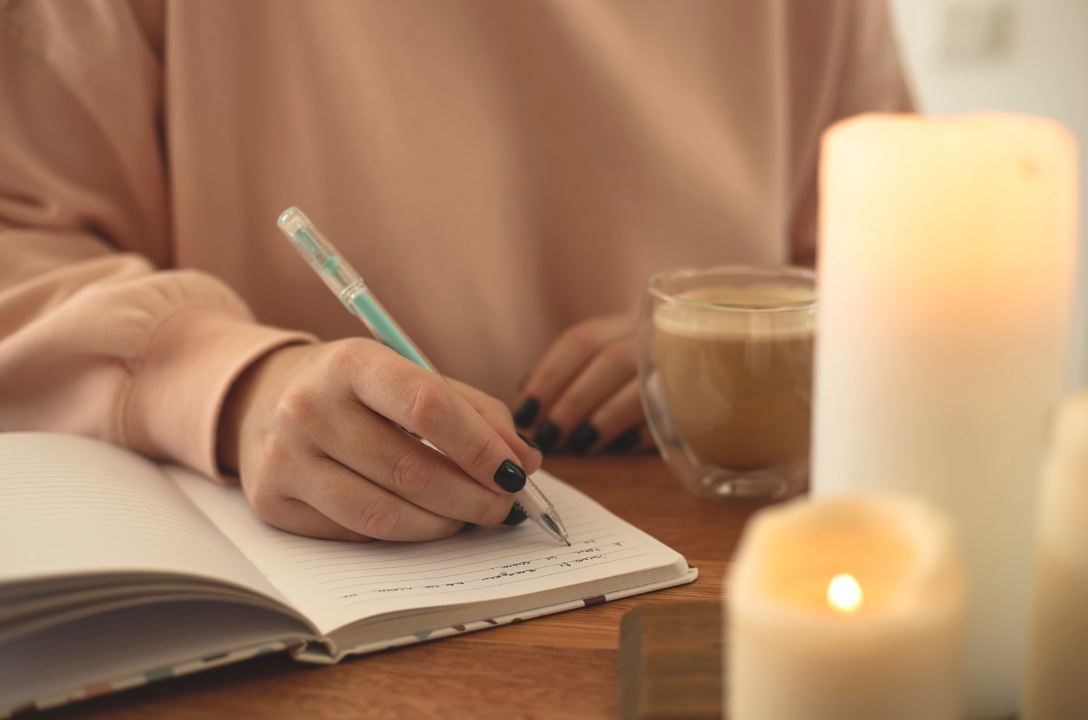 girl journalling with a coffee and a candle as a form of self-care